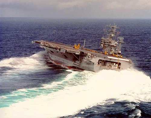 An aircraft carrier turning tightly, spray flying