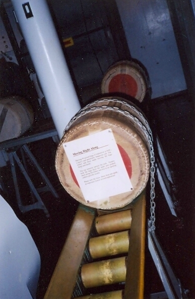 Two powder bags mounted on the conveyor with chains and red ignition pads visible in the USS North Carolina powder magazine