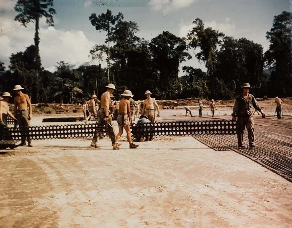 Seabees laying pierced-steel planking (Marston mat) to surface a forward airstrip in the jungle