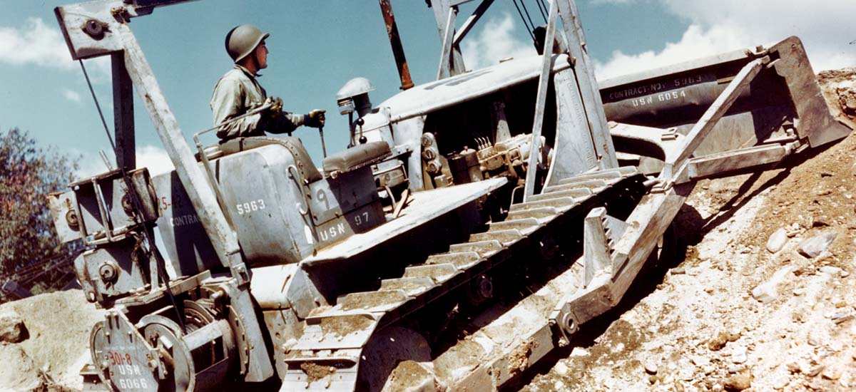 A Seabee operating a Navy bulldozer cutting a roadbed out of a hillside