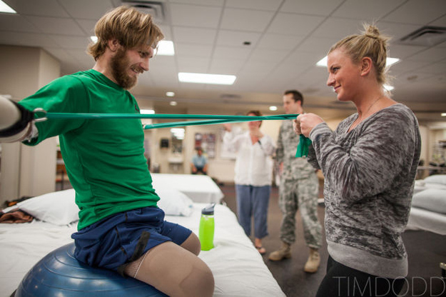Taylor Morris pulling a resistance band in physical therapy, his girlfriend holding the far end