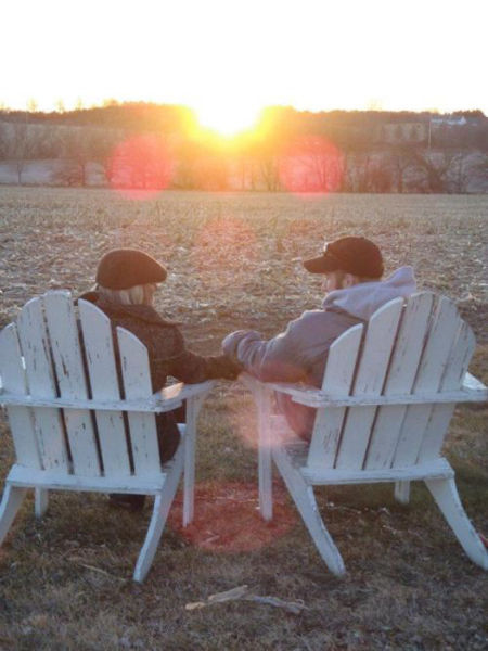 Taylor Morris and his wife holding hands between two chairs, facing a sunset over an open field