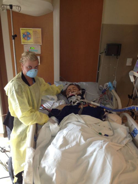 Taylor Morris on a ventilator in intensive care, his girlfriend in gown and mask standing at the bedside