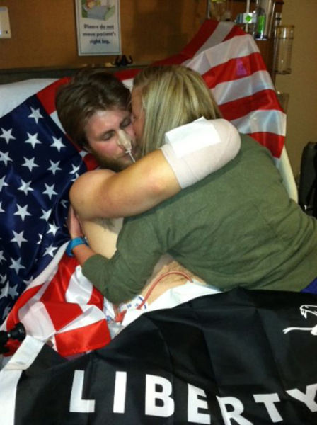 Taylor Morris held in his hospital bed by his girlfriend, an American flag spread across the blankets