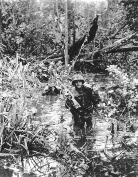 US Marines carry weapons overhead through wetland at Cape Gloucester January 1944