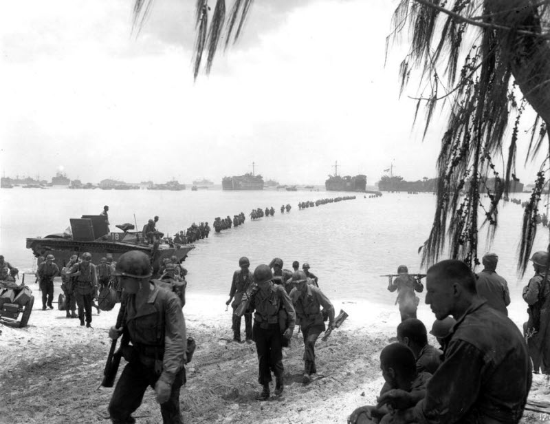 US Army reinforcement troops disembark from LSTs and cross coral reef toward Saipan beach July 1944