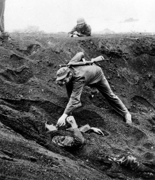 US Marine approaches Japanese soldier buried in shell hole on Iwo Jima March 1945